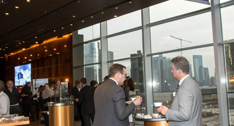 A sleek conference hall in London with navy and gold signage, a speaker on stage, and attendees networking with drinks, captured from a low angle showing the elegant décor.