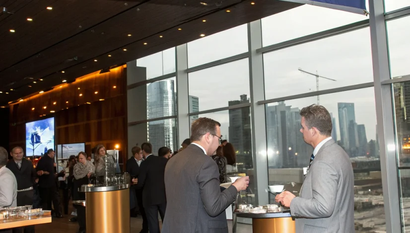 A sleek conference hall in London with navy and gold signage, a speaker on stage, and attendees networking with drinks, captured from a low angle showing the elegant décor.